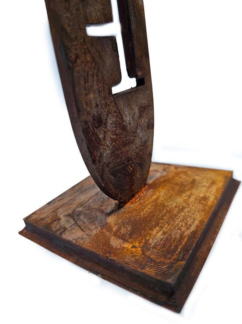 May include: A rustic wooden sculpture featuring a stylized letter 'I' cut out of a dark brown, textured piece. The sculpture is mounted on a rectangular base, also made of wood, with a similar aged appearance. The overall design has a natural, handcrafted feel.