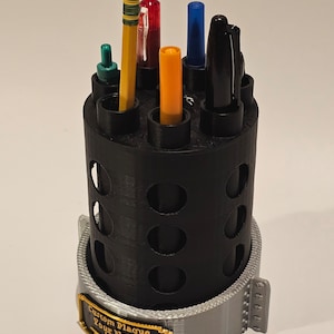 May include: Black plastic pencil holder with a gray base and a gold plaque that says "Custom Plaque Your Name". The holder has multiple slots for pens and pencils. There are six writing utensils in the holder, including a red pen, a blue pen, a yellow highlighter, a green pen, a black pen, and a yellow pencil.
