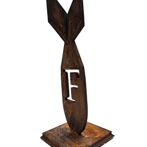 May include: A brown, stylized metal sculpture of a bomb shape with the letter "F" cut out. The sculpture has a textured finish and is mounted on a square base. The sculpture is a decorative item.