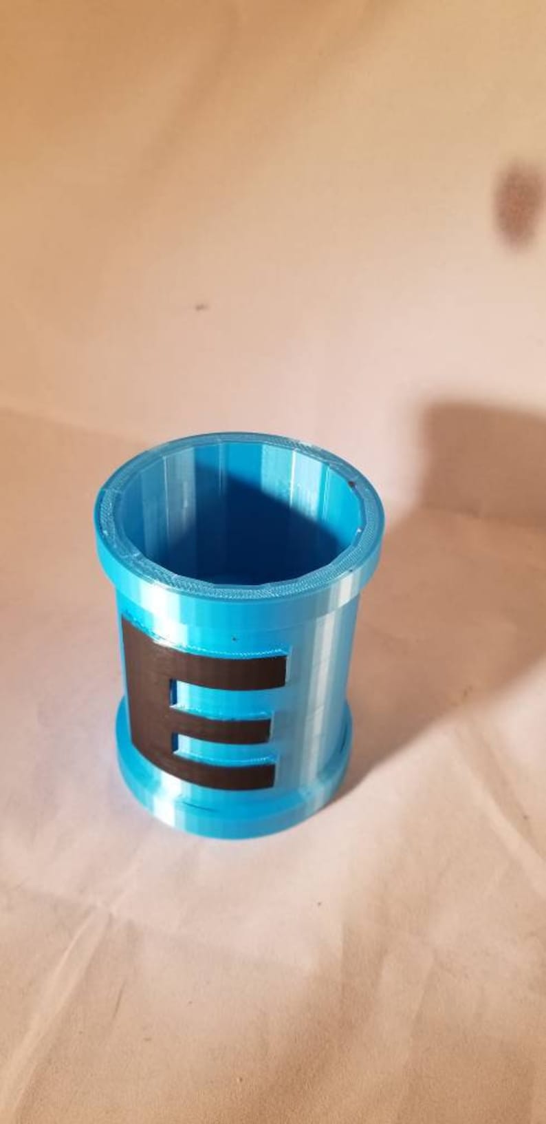 May include: A blue plastic cup with a black letter "E" printed on the side.