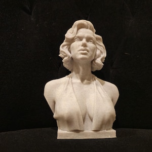 May include: A white bust sculpture of a woman with short, wavy hair. The sculpture is wearing a low-cut, sleeveless dress.