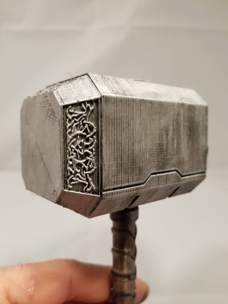 Op de afbeelding: Een zilverkleurige 3D-geprinte replica van Thor's hamer, Mjolnir, met ingewikkelde details en een textuur.
