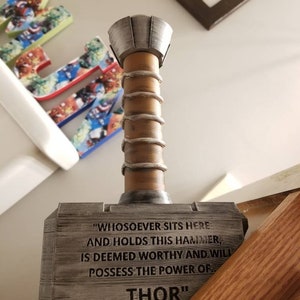 May include: A wooden replica of Thor's hammer, Mjolnir, with a silver metal top. The hammer has a quote engraved on the side: "Whosoever sits here and holds this hammer, is deemed worthy and will possess the power of Thor."