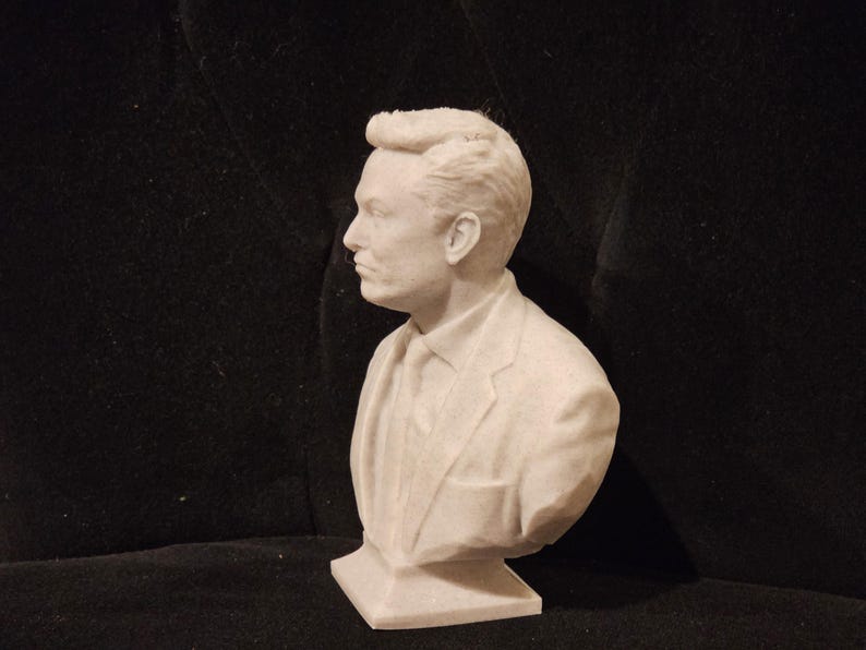 May include: A white bust sculpture of a person with short, styled hair. The person is wearing a suit jacket and a tie. The bust is on a white base.