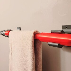 May include: A red and gray towel rack with a towel hanging on it. The towel rack is mounted to a white wall.