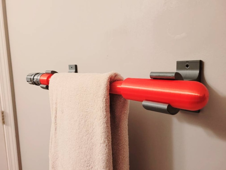 May include: A red and gray towel rack with a towel hanging on it. The towel rack is mounted to a white wall.
