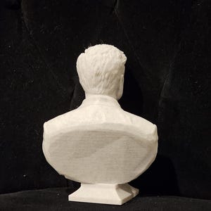 May include: White plaster bust of a person's head and shoulders, viewed from the back. The bust is on a square base.