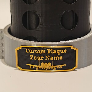 May include: A black and gold custom plaque with the text "Custom Plaque Your Name" and a decorative design.