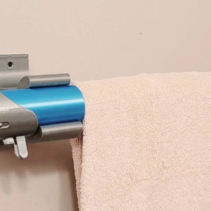 May include: A silver and blue lightsaber-style towel rack mounted on a white wall. The rack has a towel hanging on it.
