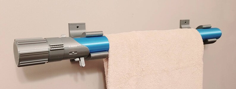 May include: A silver and blue lightsaber-style towel rack mounted on a white wall. The rack has a towel hanging on it.
