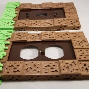 May include: Two 3D printed wall plates, one with a single light switch and the other with a double outlet. The plates are brown and have a textured design resembling a Minecraft block. The edges of the plates are green and resemble grass.