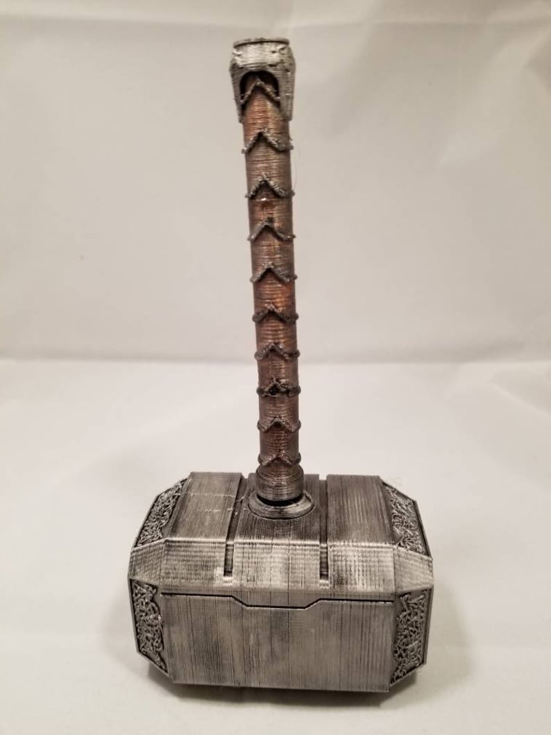 Op de afbeelding: Een zilverkleurige Mjolnir-hamerreplica met een bruine houten handgreep. De hamer heeft ingewikkelde details en een getextureerd oppervlak.