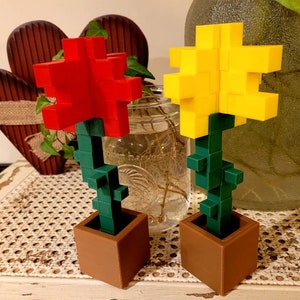 May include: Two small potted plants with red and yellow flowers. The flowers are made of plastic blocks and resemble pixelated flowers.