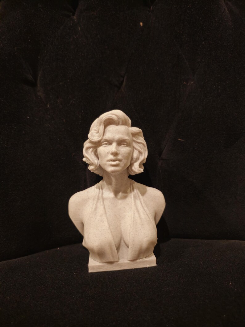 May include: A white bust sculpture of a woman with short, wavy hair. The sculpture is wearing a low-cut, sleeveless dress.