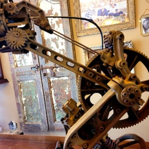 Puede incluir: Primer plano de una escultura de metal de estilo steampunk con engranajes y pi&ntilde;ones. La escultura est&aacute; pintada en un color marr&oacute;n oxidado y tiene un acabado desgastado. La escultura est&aacute; hecha de metal y tiene un dise&ntilde;o complejo.