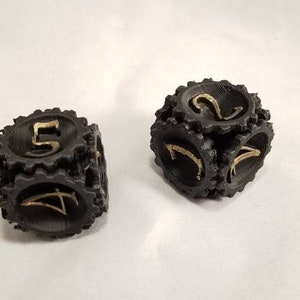 May include: Two black dice with gold numbers. The dice are in focus and have a textured surface. The dice are on a white background.