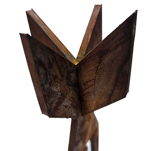 May include: A carved wooden sculpture featuring a starburst design. The sculpture is made of dark brown wood with visible grain and texture. The starburst has five points, and the base is a carved figure.