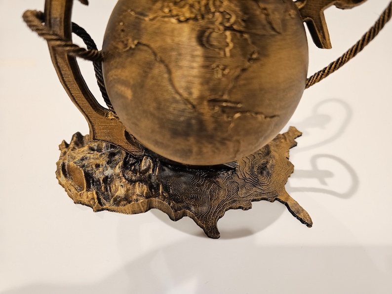 May include: A wooden globe with a rope handle and an anchor base. The globe is brown and has a textured surface. The base is shaped like a continent.