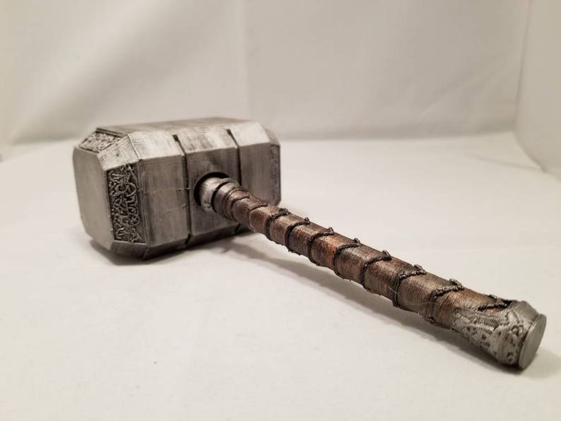 Op de afbeelding: Een zilveren en bruine hamer met een gedetailleerd ontwerp. De hamer heeft een lange steel met een gevlochten touwontwerp.
