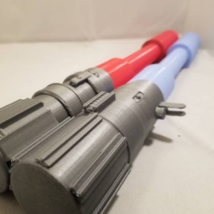 May include: Two toy lightsabers. One has a gray handle with a red blade, and the other has a gray handle with a light blue blade. The handles have detailed designs and are made of a metallic-looking material.