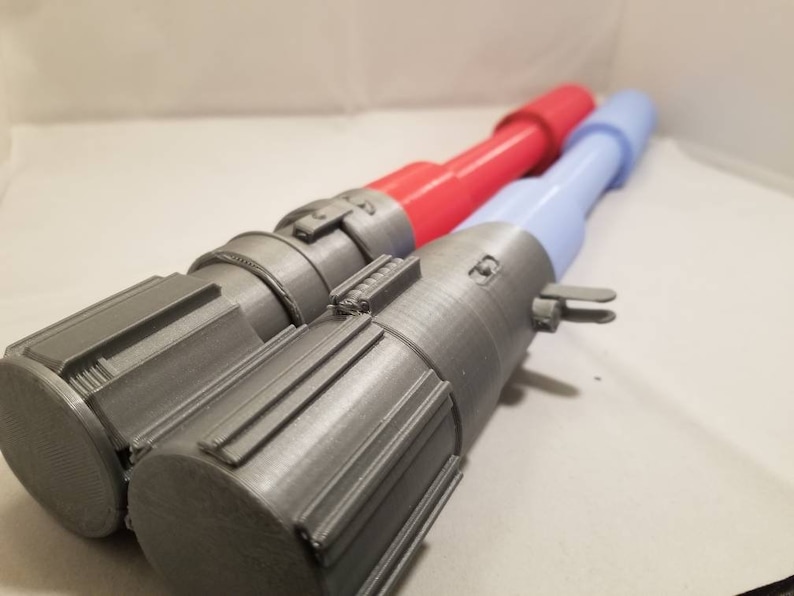 May include: Two toy lightsabers. One has a gray handle with a red blade, and the other has a gray handle with a light blue blade. The handles have detailed designs and are made of a metallic-looking material.