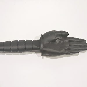 May include: A black 3D printed hand with a black handle attached to the wrist. The hand is open and the fingers are spread apart.