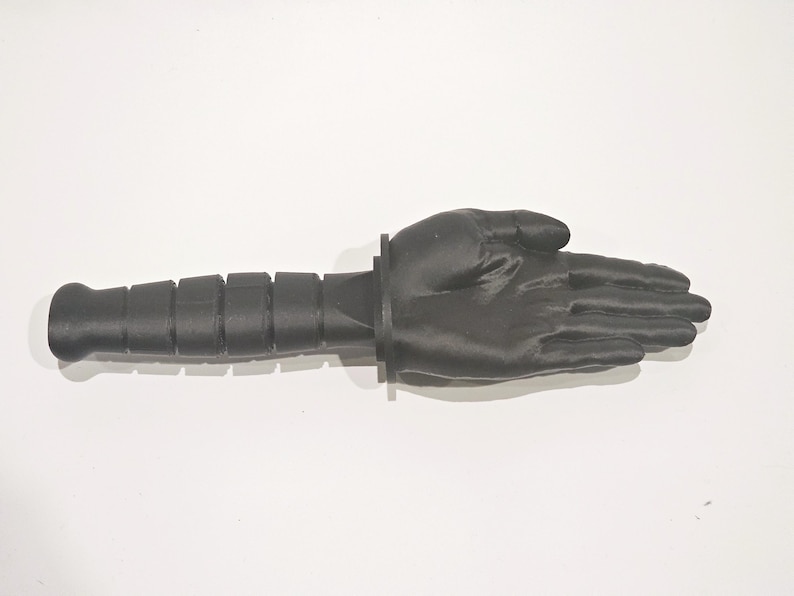 May include: A black 3D printed hand with a black handle attached to the wrist. The hand is open and the fingers are spread apart.