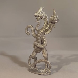 May include: A silver metal miniature of a two-headed dragon with a curled tail. The dragon is standing on a small base.
