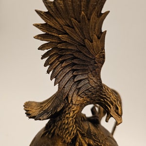 May include: A gold-colored eagle sculpture with its wings spread out, perched atop a globe. The eagle's head is turned to the side, and its talons are gripping the globe.
