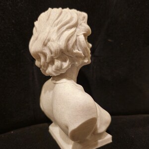 May include: A white bust sculpture of a person with short, wavy hair. The bust is on a square base.