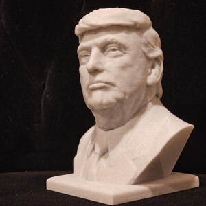 May include: A white bust sculpture of a man with short, combed-over hair. The sculpture is on a white base.