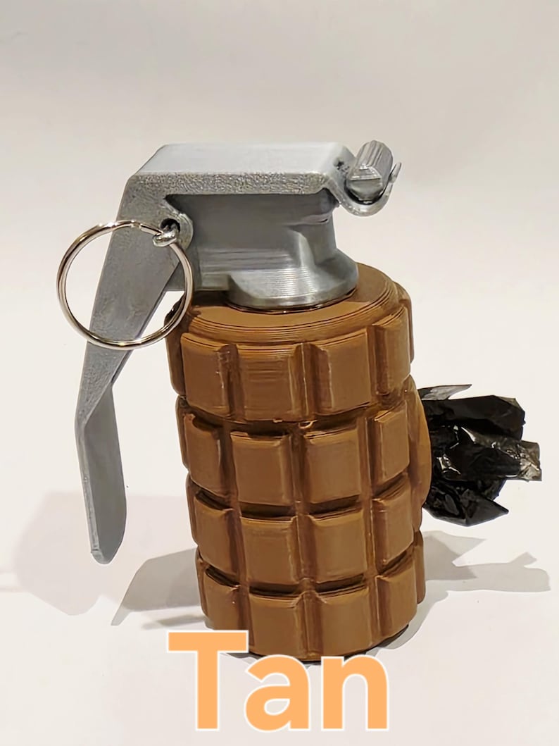 May include: A tan-colored grenade with a silver-colored top and pull ring. The body of the grenade has a textured, block-like design. The word "Tan" is written in orange at the bottom of the image.