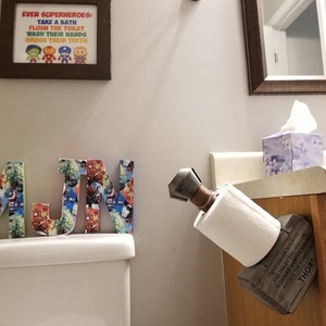 May include: A wooden toilet paper holder shaped like Thor's hammer, with the inscription "Whosoever holds this hammer, if he be worthy, shall possess the power of Thor."  The holder is mounted on a wooden cabinet.