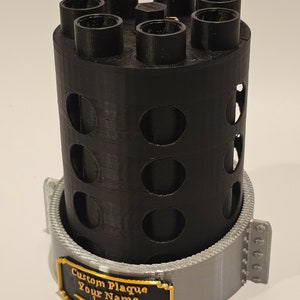 May include: A black 3D printed cylinder with a silver base and a gold plaque that reads "Custom Plaque Your Name". The cylinder has multiple holes around the sides and top.