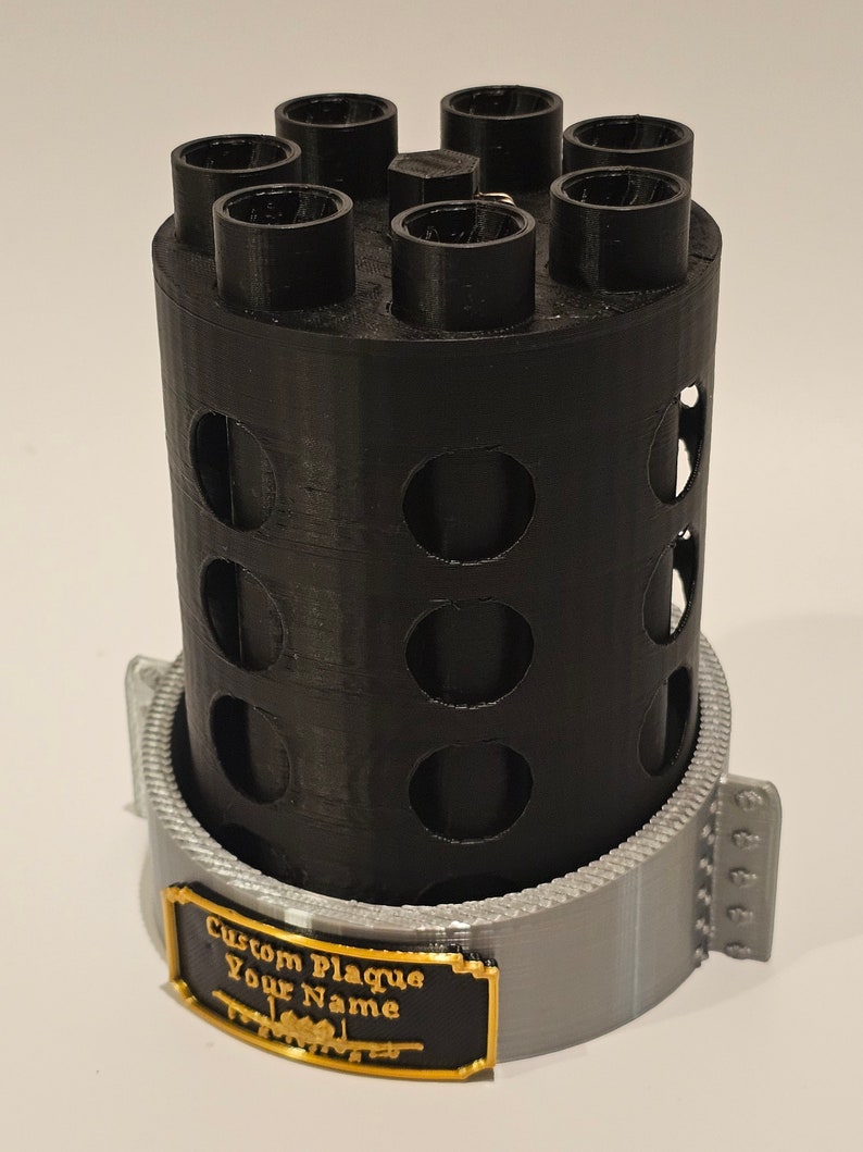 May include: A black 3D printed cylinder with a silver base and a gold plaque that reads "Custom Plaque Your Name". The cylinder has multiple holes around the sides and top.