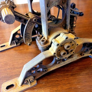 Puede incluir: Primer plano de una base de l&aacute;mpara de madera de estilo steampunk con un engranaje, una palanca y un interruptor "OFF ON". La base est&aacute; pintada en un acabado desgastado marr&oacute;n y dorado.