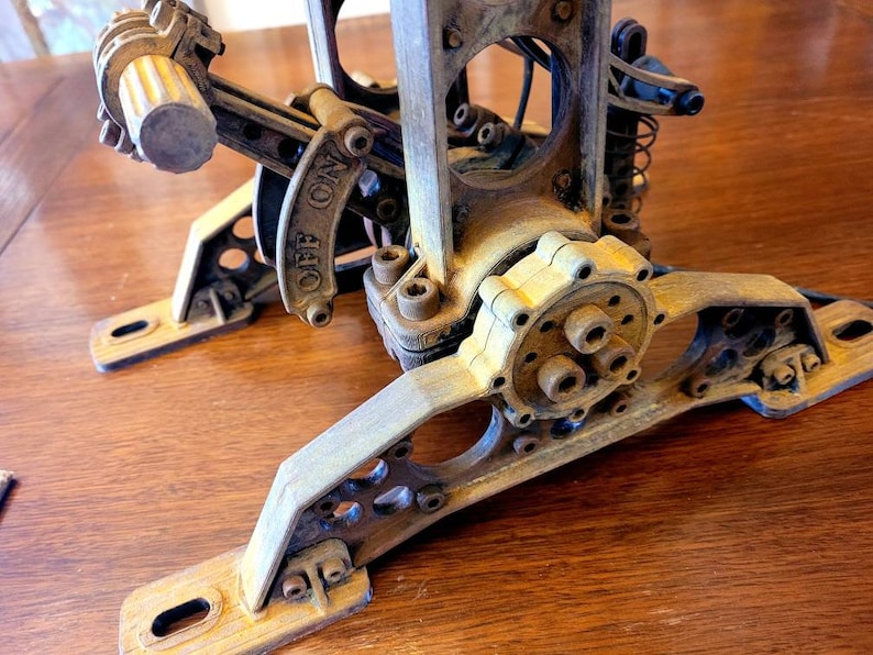 Puede incluir: Primer plano de una base de l&aacute;mpara de madera de estilo steampunk con un engranaje, una palanca y un interruptor "OFF ON". La base est&aacute; pintada en un acabado desgastado marr&oacute;n y dorado.