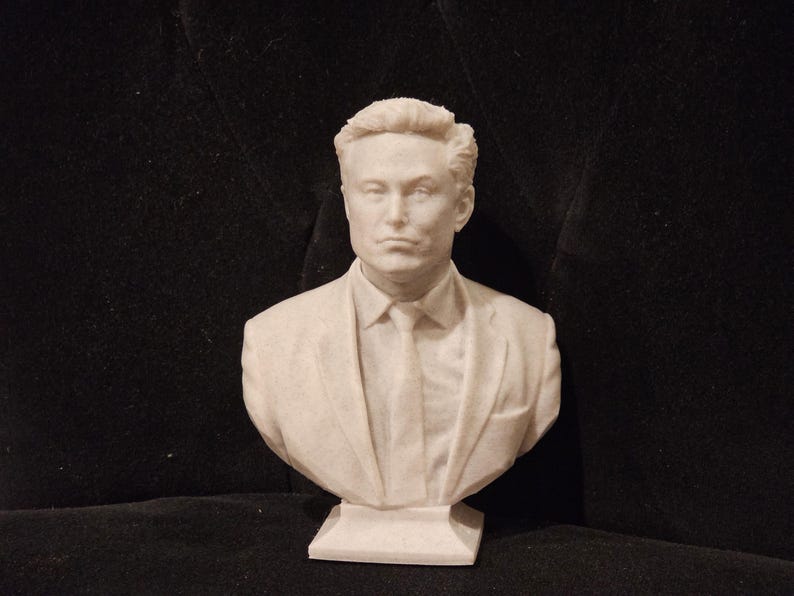 May include: A white bust sculpture of a person with short brown hair wearing a suit jacket and tie. The bust is on a white base.