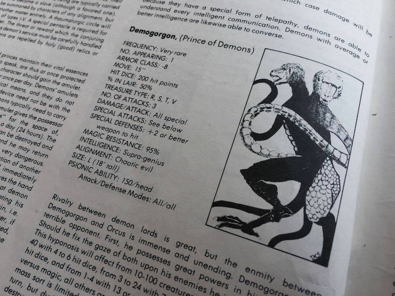 May include: Black and white illustration of a three-headed demon with a scaly tail. The demon is called Demogorgon, Prince of Demons. The text describes the demon's frequency, armor class, movement speed, hit dice, treasure type, number of attacks, damage per attack, special attacks, special defenses, magic resistance, intelligence, alignment, size, psionic ability, and attack/defense modes.
