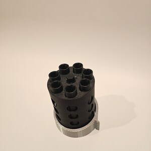 May include: A black 3D printed cylinder with eight holes around the top and a gray plastic ring around the bottom.