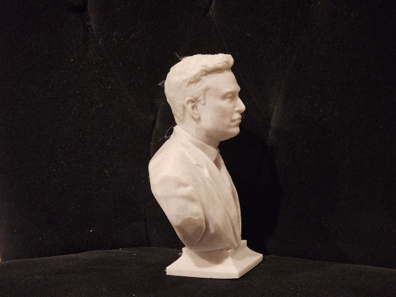 May include: A white bust sculpture of a person wearing a suit jacket. The sculpture is on a white base.