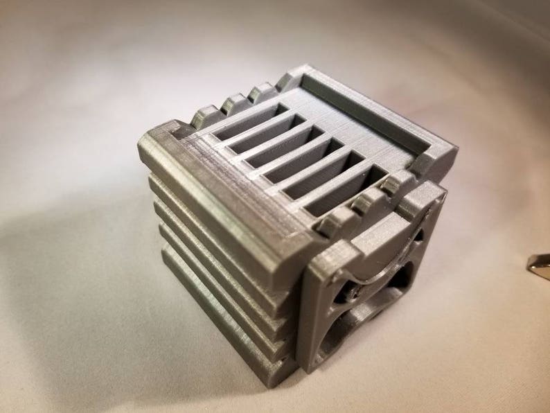 K&ouml;nnte beinhalten: Ein graues 3D-gedrucktes Objekt mit einer Reihe von Schlitzen oben und einem geschwungenen Design an der Seite.