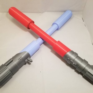 May include: Two toy lightsabers crossed. One is red with a gray handle, the other is light blue with a gray handle. The lightsabers are made of plastic and are designed to look like the iconic weapons from a science fiction franchise.