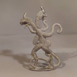 May include: A silver-colored three-headed dragon figurine with a curled tail. The dragon is standing on a small base.