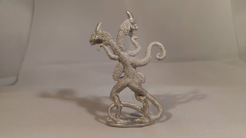May include: A silver-colored three-headed dragon figurine with a curled tail. The dragon is standing on a small base.