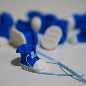May include: A close-up of a blue and white miniature shoe with a blue ribbon. The shoe is surrounded by other miniature shoes of the same design.