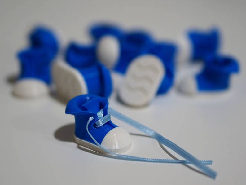 May include: A close-up of a blue and white miniature shoe with a blue ribbon. The shoe is surrounded by other miniature shoes of the same design.