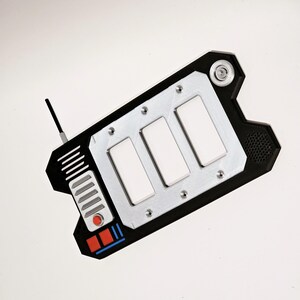 May include: A black and silver handheld device with three white buttons and a red button. The device has a small antenna and a black and blue stripe on the bottom.