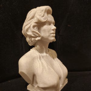 May include: A white bust sculpture of a woman with short, wavy hair. The sculpture is made of a textured material and is set on a small base.