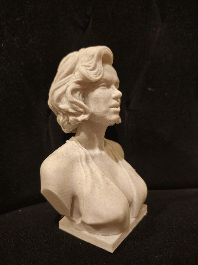 May include: A white bust sculpture of a woman with short, wavy hair. The sculpture is made of a textured material and is set on a small base.